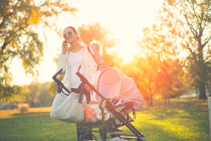 Busy babysitter talking on the phone outdoors,standing by baby stroller